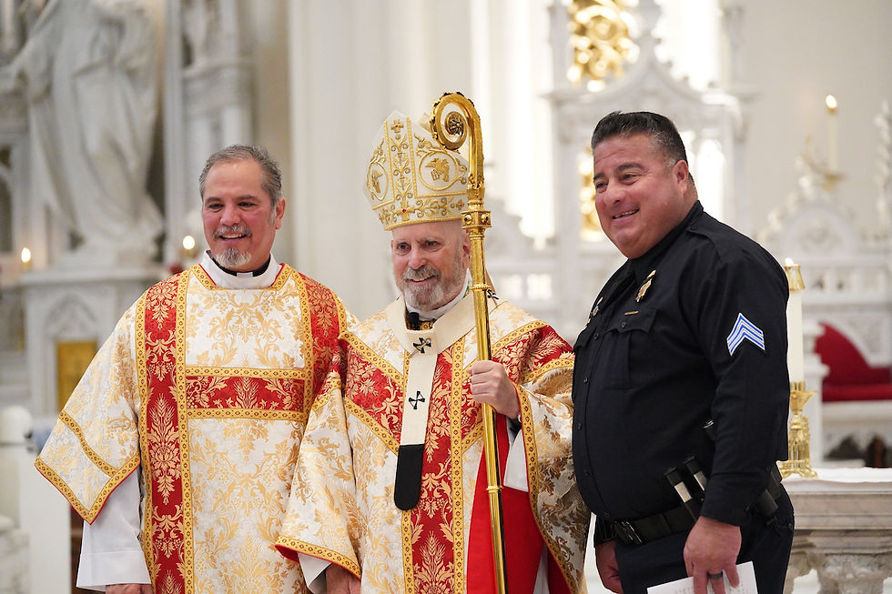 Tres hombres posan en una iglesia. Dos visten trajes religiosos rojos y dorados; el tercero lleva uniforme negro. Sonríen. Fondo blanco decorado.