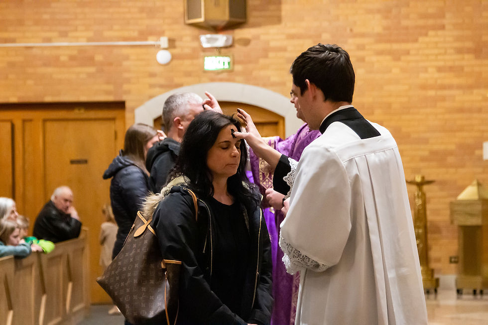 Sacerdote en sotana blanca aplica ceniza en la frente de una mujer en una iglesia de ladrillo. Fila de personas espera su turno. Atmosfera solemne.