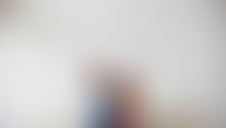 Pareja sentada de espaldas en un sofá beige, ambos con brazos cruzados. Fondo de pared blanca de ladrillo. Atmosfera tensa y seria.