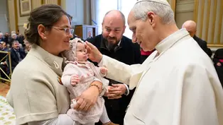 Sacerdote bendice a un bebé en brazos de una mujer. Hombre observa sonriente. Interior elegante, ambiente cálido y emotivo.