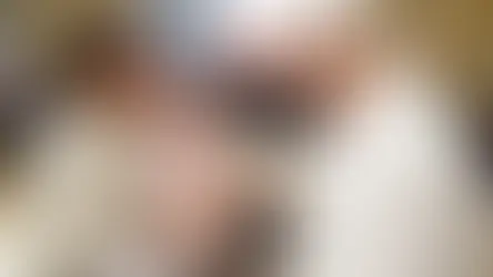 Sacerdote bendice a un bebé en brazos de una mujer. Hombre observa sonriente. Interior elegante, ambiente cálido y emotivo.