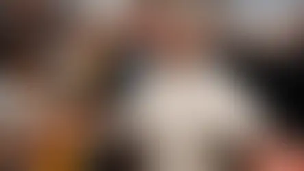 Un clérigo sonriente en túnica blanca saluda a una multitud en una iglesia grande. Personas toman fotos; ambiente alegre y colorido.
