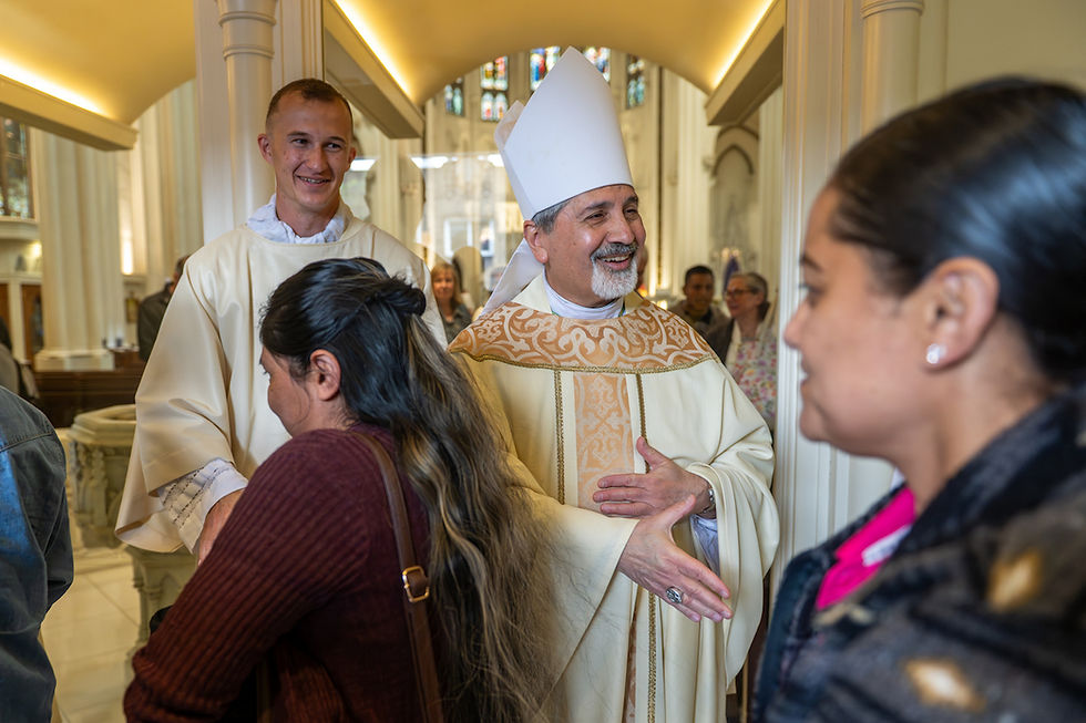 Obispo con mitra y monaguillo saludan a feligreses en una iglesia iluminada; ambiente cordial y festivo.