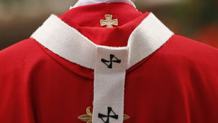 Primer plano de una vestidura roja de clérigo con estola blanca y cruces bordadas, sobre fondo desenfocado.