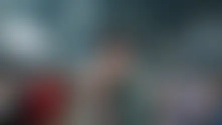 Dos personas sonríen en un estadio lleno de gente con luces brillantes. Visten de manera casual y llevan gafetes. Ambiente alegre y concurrido.