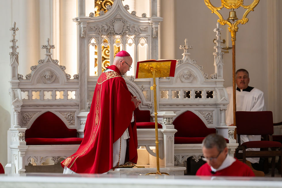 Obispo católico de rojo orando ante un atril en una iglesia ornamentada, con ayudantes al fondo y ambiente solemne.