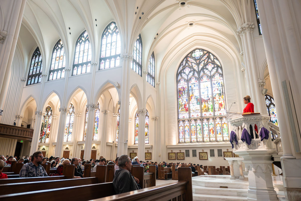 Vista amplia del interior de una catedral con vitrales mientras una lectora proclama desde el ambón durante la liturgia.