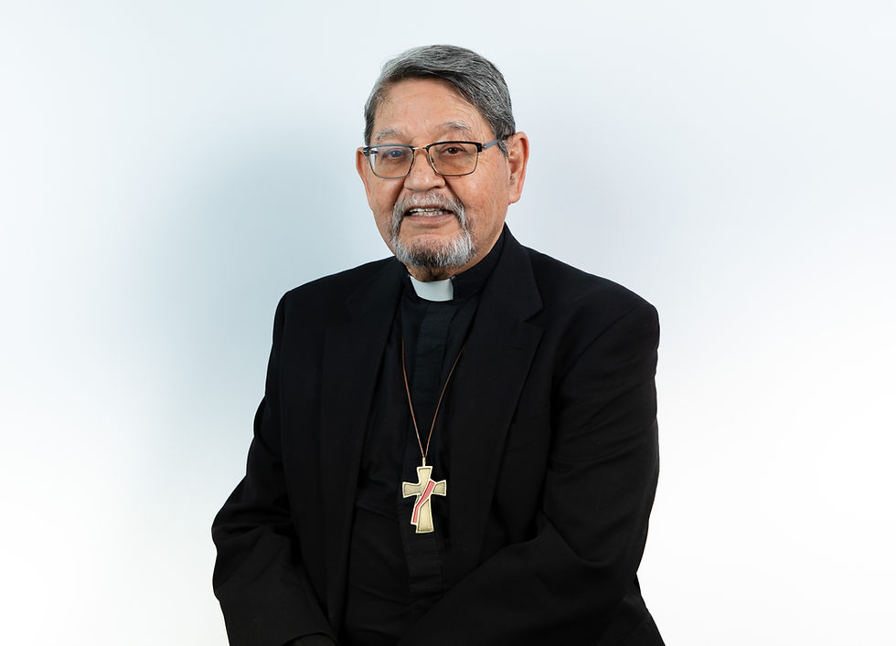 Hombre mayor con gafas y barba, vestido de sacerdote con cruz dorada. Fondo blanco. Expresión amable. Traje negro formal.