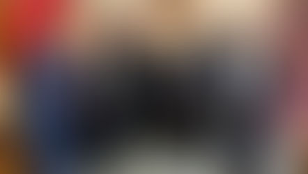 Seis sacerdotes y un hombre de traje posan sonrientes en una oficina con libros rojos y cuadros religiosos.
