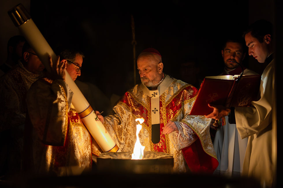 Obispo con vestiduras doradas y rojas bendice el fuego durante la Vigilia Pascual, mientras el clero sostiene el cirio pascual y el libro litúrgico.