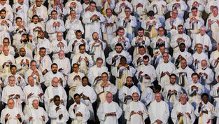 Sacerdotes en ropas blancas realizan un gesto de oración en grupo, mostrando concentración y solemnidad. Fondo oscuro y uniforme.