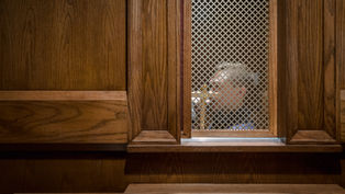 Persona en un confesionario visto a través de una rejilla, en una cabina de madera. Ambiente solemne y tranquilo. Sin texto visible.