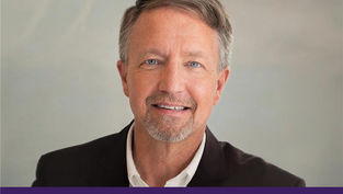 Hombre sonriente con barba, fondo gris claro. Lleva traje oscuro y camisa blanca. Texto: "Appeal in Action" en fondo morado.