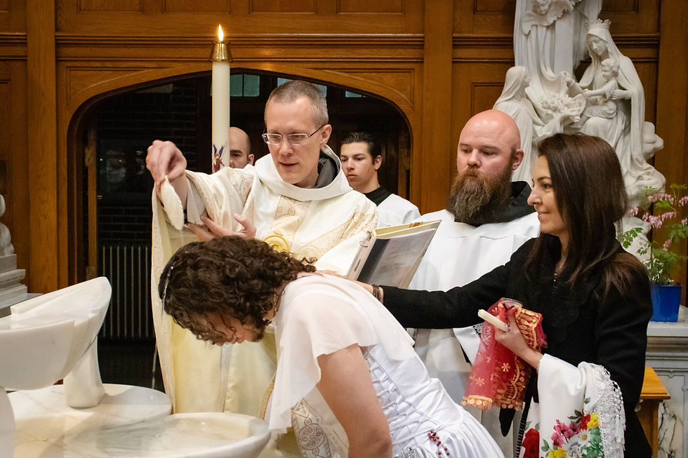 Sacerdote vierte agua sobre una mujer inclinada durante un bautizo, con velas y una estatua religiosa de fondo.