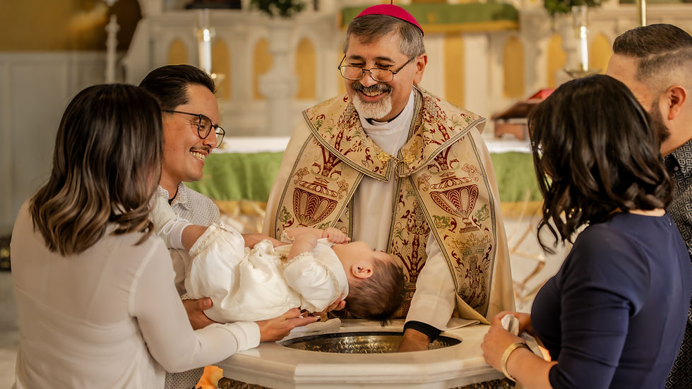 Sacerdote sonriente bautiza a un bebé vestido de blanco, sostenido por familiares, en una iglesia iluminada.