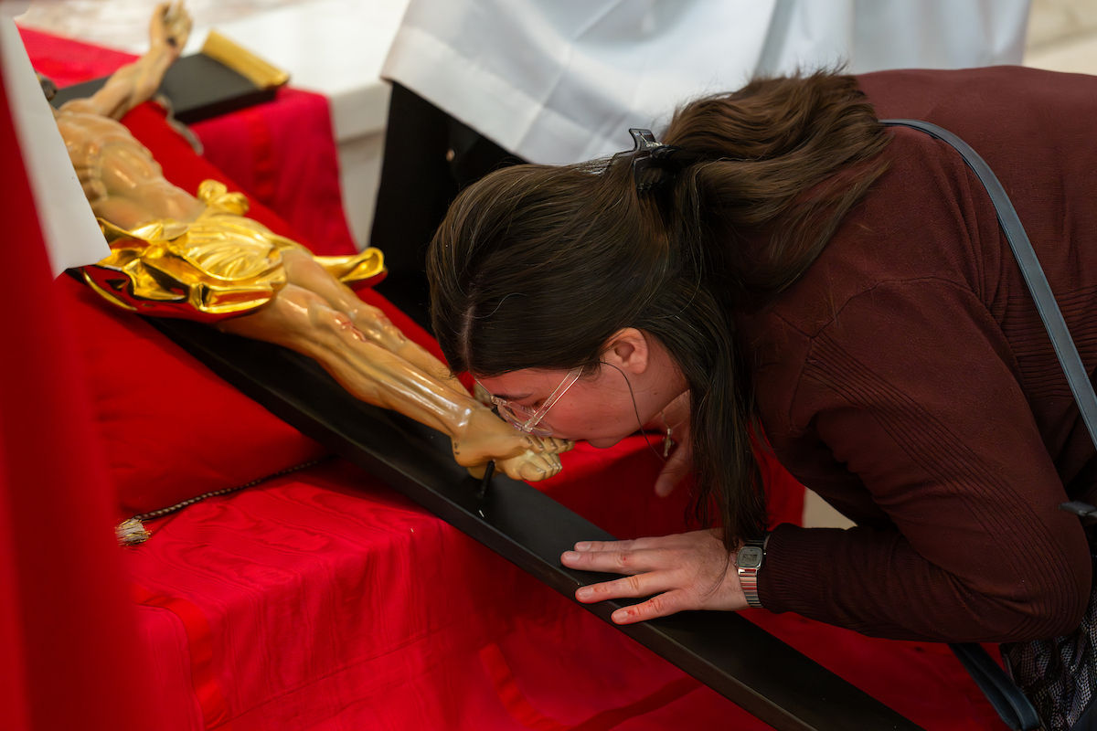 Una mujer besa con reverencia los pies de un crucifijo colocado sobre una tela roja durante la veneración de la cruz.