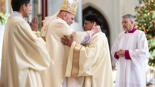 Obispo y sacerdote abrazándose en una ceremonia religiosa. Fondo de iglesia decorada, vestimenta blanca y dorada. Atmosfera solemne.