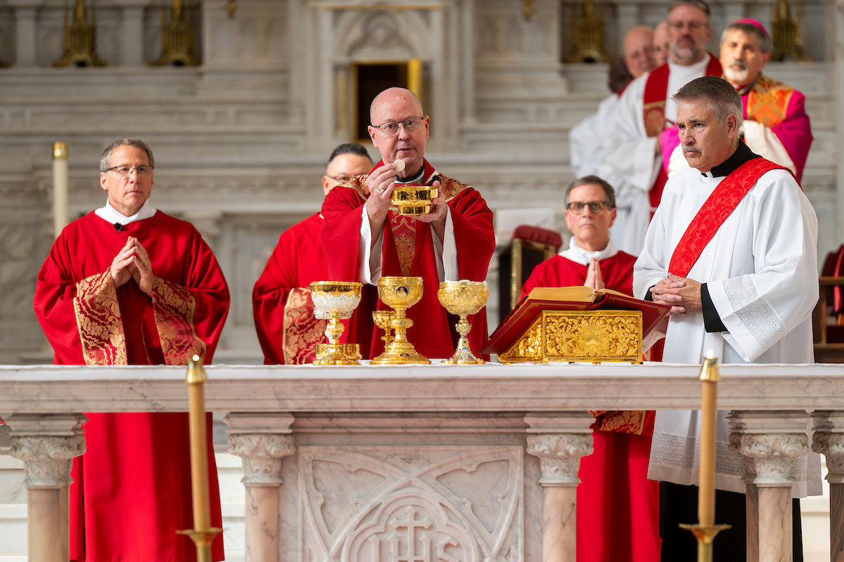 Un sacerdote eleva la hostia sobre el altar durante la liturgia del Viernes Santo, rodeado de otros clérigos.
