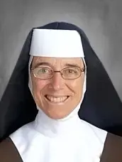 Monja sonriente con hábito blanco y velo negro, de frente sobre fondo gris.
