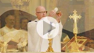 Obispo en misa levantando hostia, rodeado de objetos dorados y una cruz. Ambiente solemne en iglesia, asistentes en sotanas blancas.
