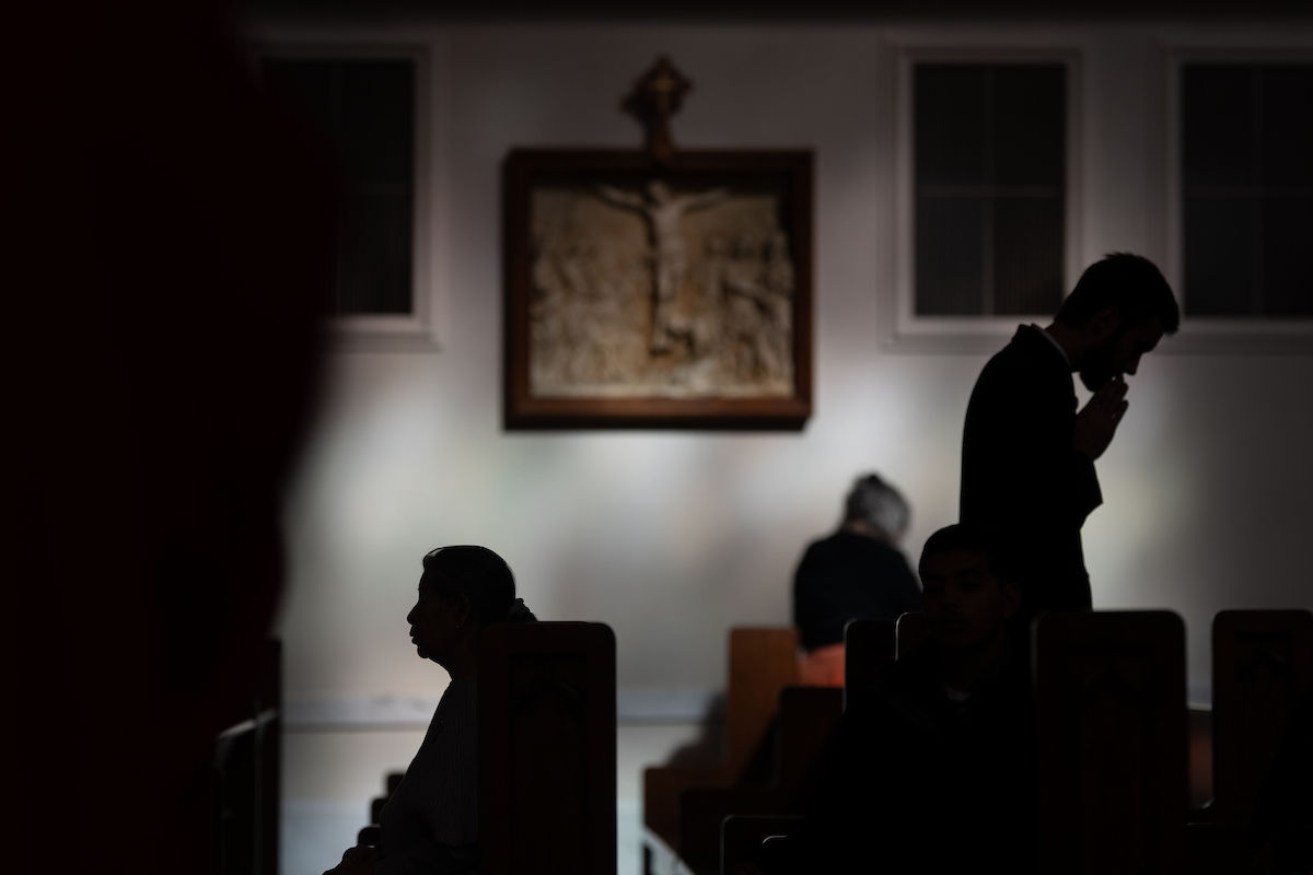 Fieles en silueta rezan en silencio en los bancos de una iglesia con poca iluminación.