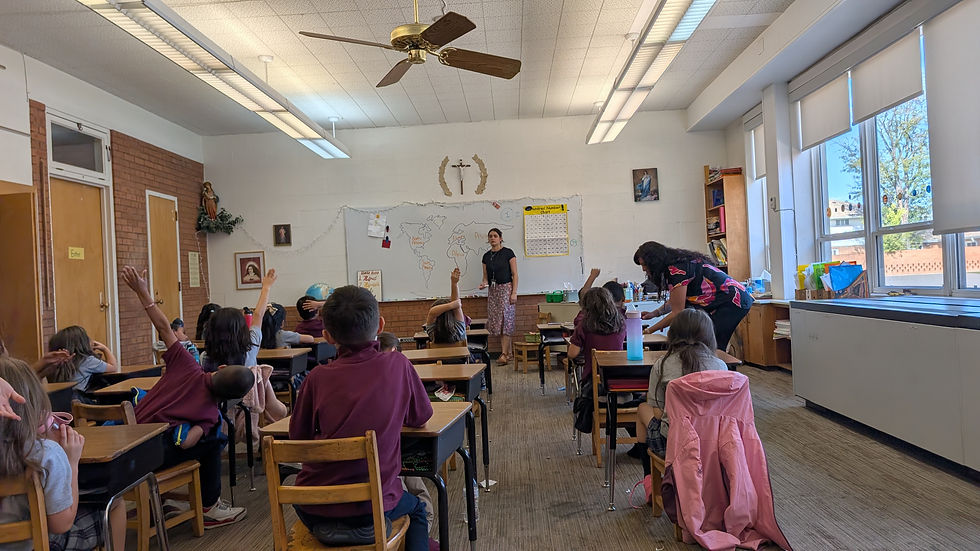 Aula con alumnos levantando la mano y una maestra frente a un mapa en la pizarra. Ambiente acogedor, ventanas grandes, decoración religiosa.