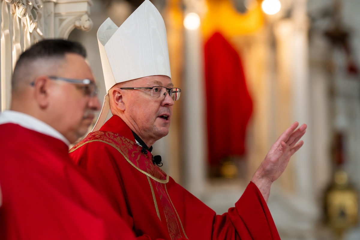 Un obispo con mitra blanca hace un gesto mientras habla durante la liturgia del Viernes Santo.