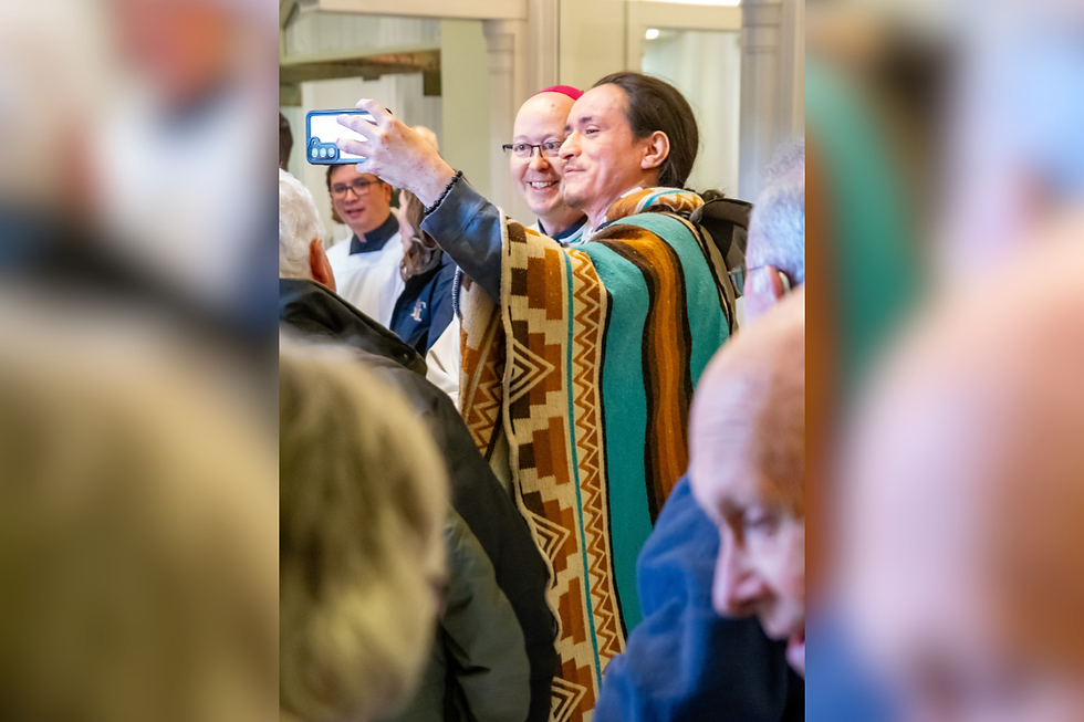 Hombre con poncho colorido se toma una selfie sonriente entre una multitud en interiores.