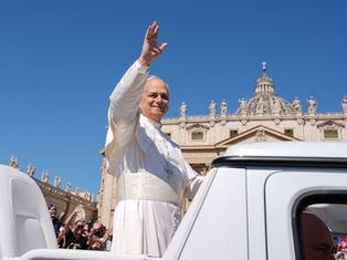 El papa sonriente saluda desde un vehículo blanco en la Plaza de San Pedro, con la basílica al fondo y cielo azul.