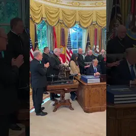 Trump reza en el Despacho Oval con varios obispos; fondo con cortinas doradas y banderas.