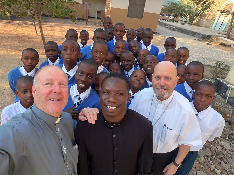 Grupo de escolares sonrientes con dos sacerdotes posando al aire libre en un patio escolar.
