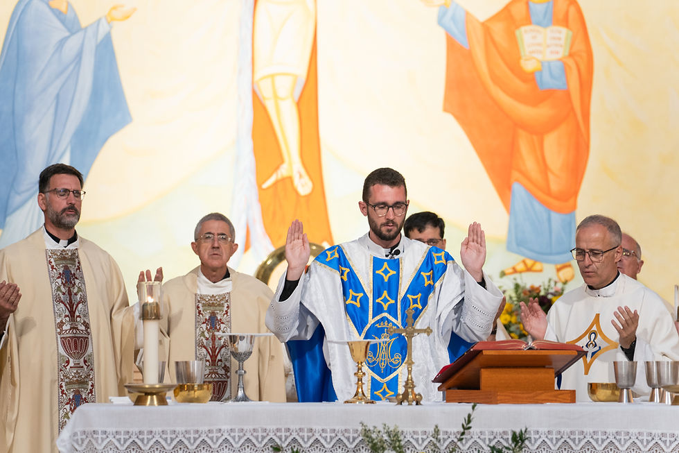 Misa con cuatro sacerdotes orando ante el altar; uno viste casulla azul. Fondo con mural religioso en tonos azul y naranja.