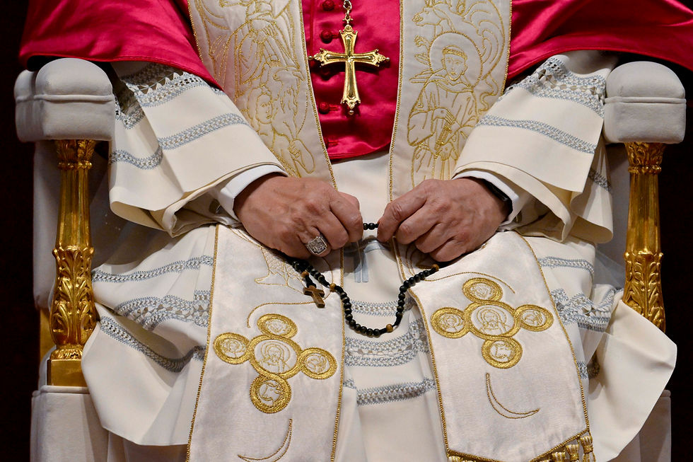 Pope con vestiduras blancas y cruz dorada, sentado, sosteniendo un rosario negro; detalles bordados en oro.