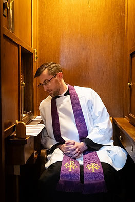Sacerdote sentado en un confesionario de madera, vistiendo sotana blanca y estola morada. Ambiente tranquilo e introspectivo.