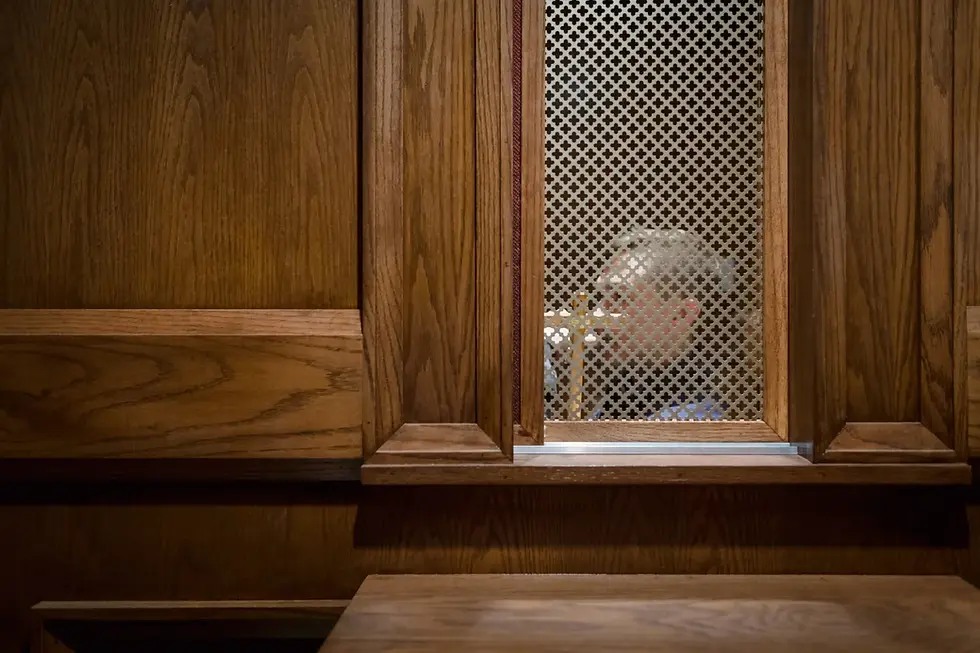 Persona en un confesionario visto a través de una rejilla, en una cabina de madera. Ambiente solemne y tranquilo. Sin texto visible.